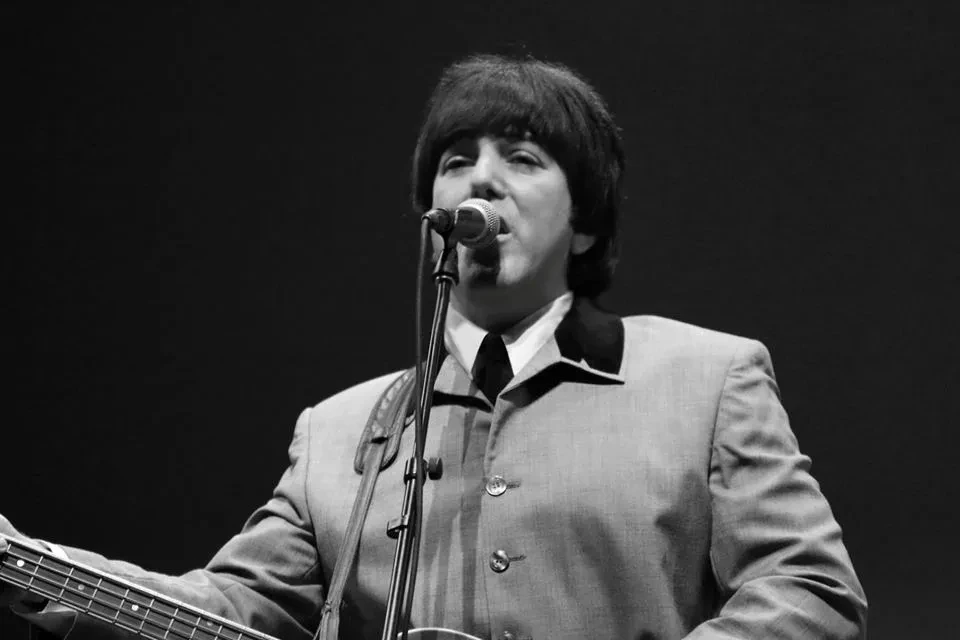 Fab 5 bassist singing at microphone in black and white collarless suit