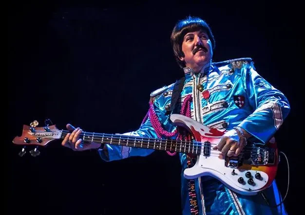 Fab 5 member in Sgt. Pepper blue costume playing bass guitar